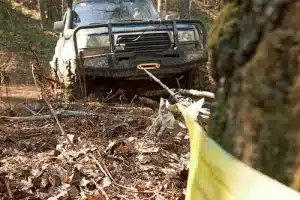 Are Off-Road Accessories & Modifications Necessary? | Outlander Motorsports in Martinez, CA. Image of a 4x4 off-road vehicle pulling itself with the help of a winch, clinging to a tree.