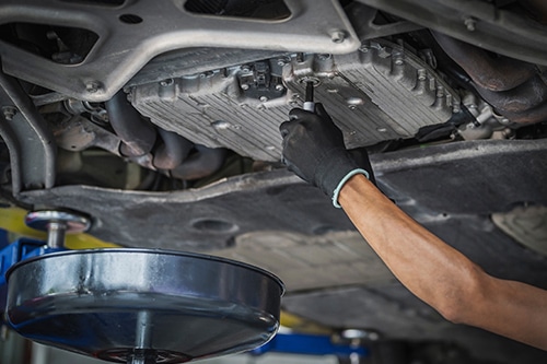 Expert Oil Change Services in Martinez, CA | Outlander Motorsports. Image of mechanic arm tightening oil drain plug on car in shop.