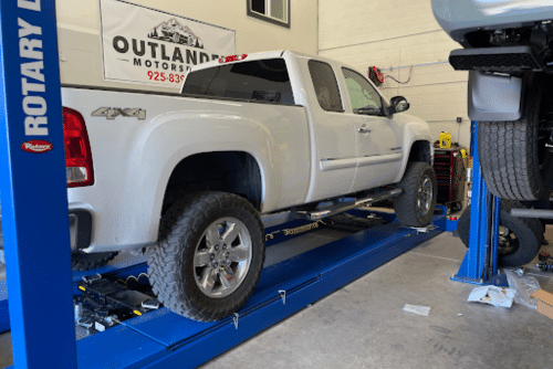 Road force balancing in Martinez, CA at Outlander Motorsports. Image of white chevy 4x4 pick up on lift to get tires balanced in shop.