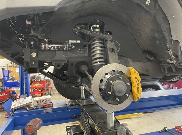 Vehicle underside with FOX shock absorber and Brembo brake caliper in a workshop setting.