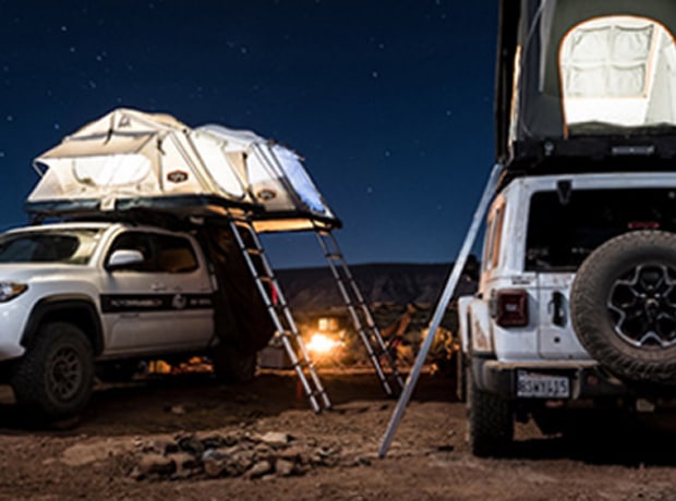 Two vehicles with rooftop tents in a desert landscape under a starry night sky.