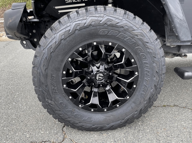 Close-up of a black off-road vehicle tire with deep treads and a glossy black alloy wheel.