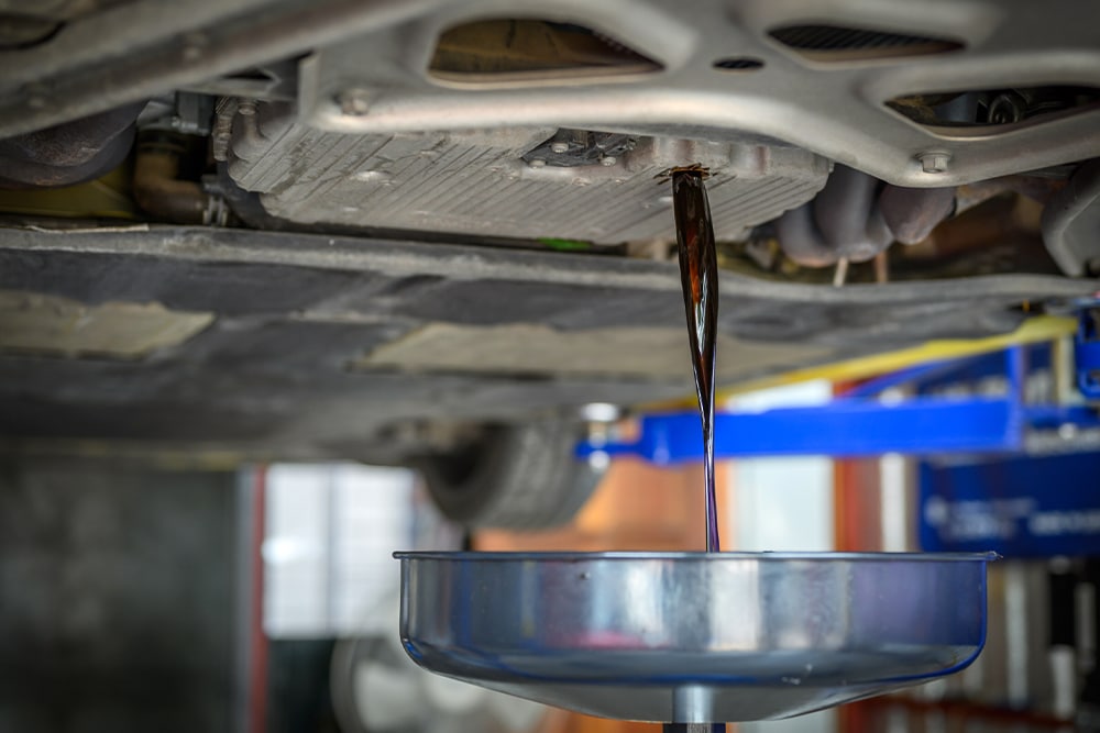 Fluid exchange services for cars, trucks, SUVs, 4X4 and Off Road vehicles in Martinez, CA with Outlander Motorsports. Image of transmission fluid being drained into fluid catch pan from car that is on a lift in the shop.