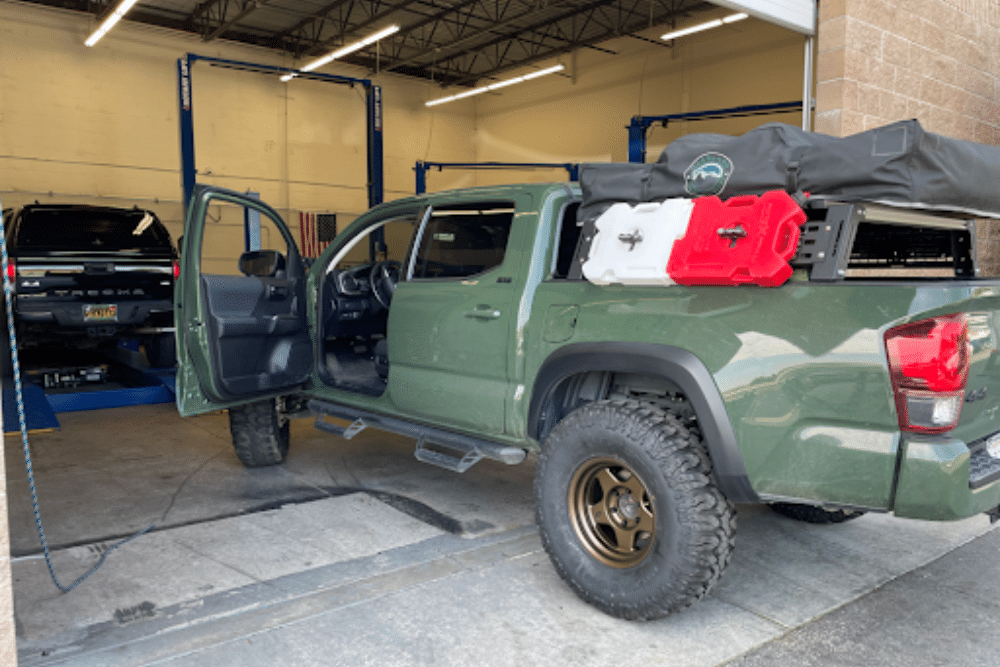 Ultimate Overland Truck Upgrades in Martinez, CA by Outlander Motorsports. Green Toyota Tacoma with overland modifications, including water storage tanks, parked inside a shop