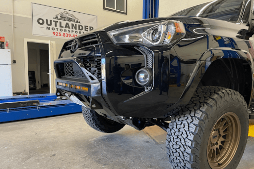 Top Off-Road Modifications for Fall Adventures in California. A black Toyota vehicle with a custom front bumper, lifted suspension, and aggressive off-road tires, in the Outlander Motorsports shop.