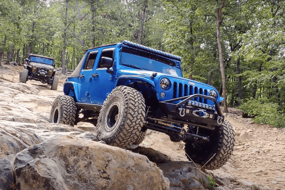 off-road trails, Off Road Specialist in Martinez, CA at Outlander Motorsports. A rugged blue Jeep with off-road modifications climbing over rocky terrain.