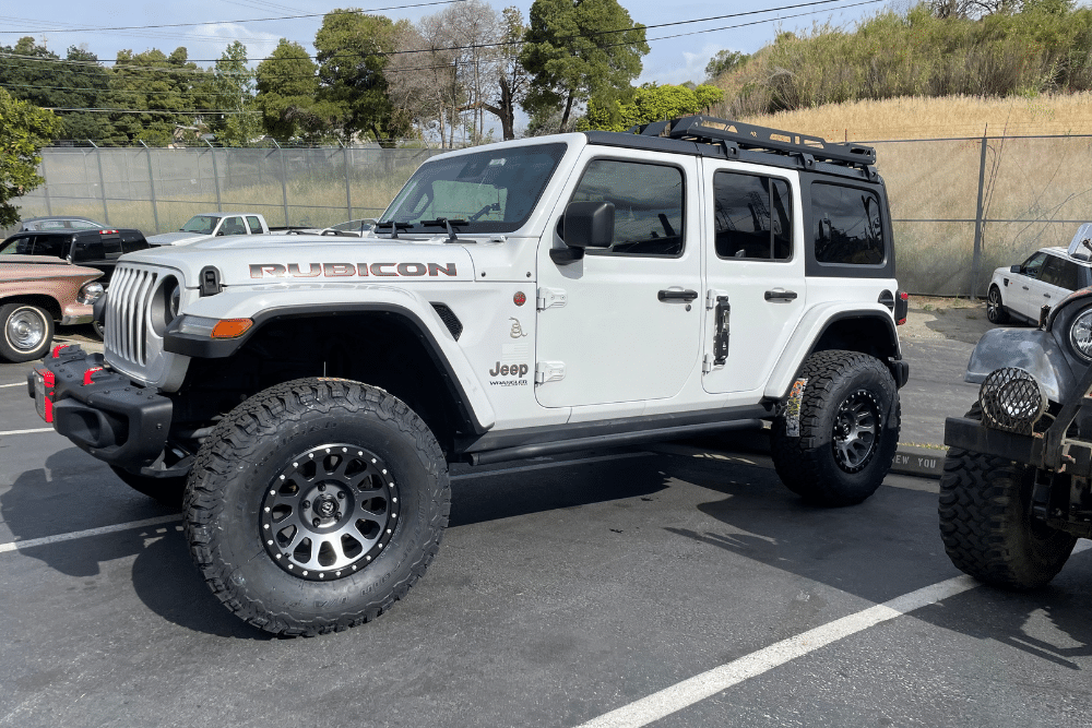 off-road pitfalls, Off Road Specialist in Martinez, CA at Outlander Motorsport. Lifted white Jeep Wrangler Rubicon with aftermarket wheels and a roof rack parked outdoors. Ideal for showcasing off-road customization and Jeep upgrade services.